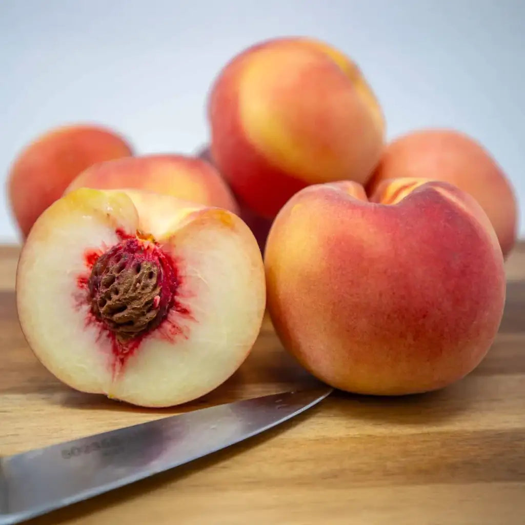 Babcock Peaches on a wooden cutting board with one sliced open sold by Paradise Nursery
