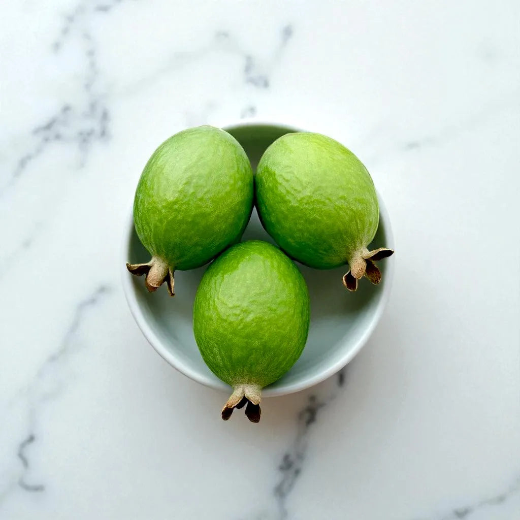 Three green pineapple guavason a small white plate with a marble background