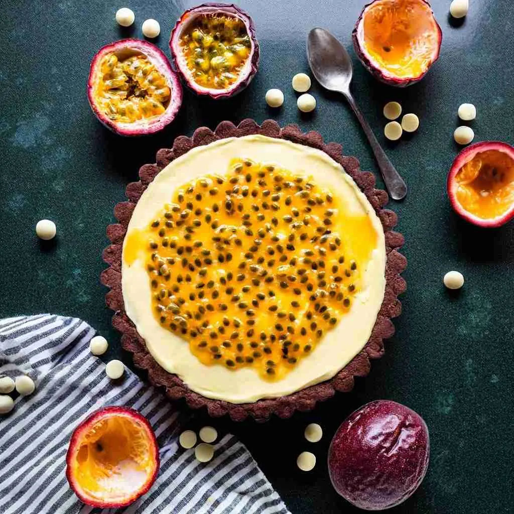 Passion fruit tart with passion fruits and white chocolate on a dark surface